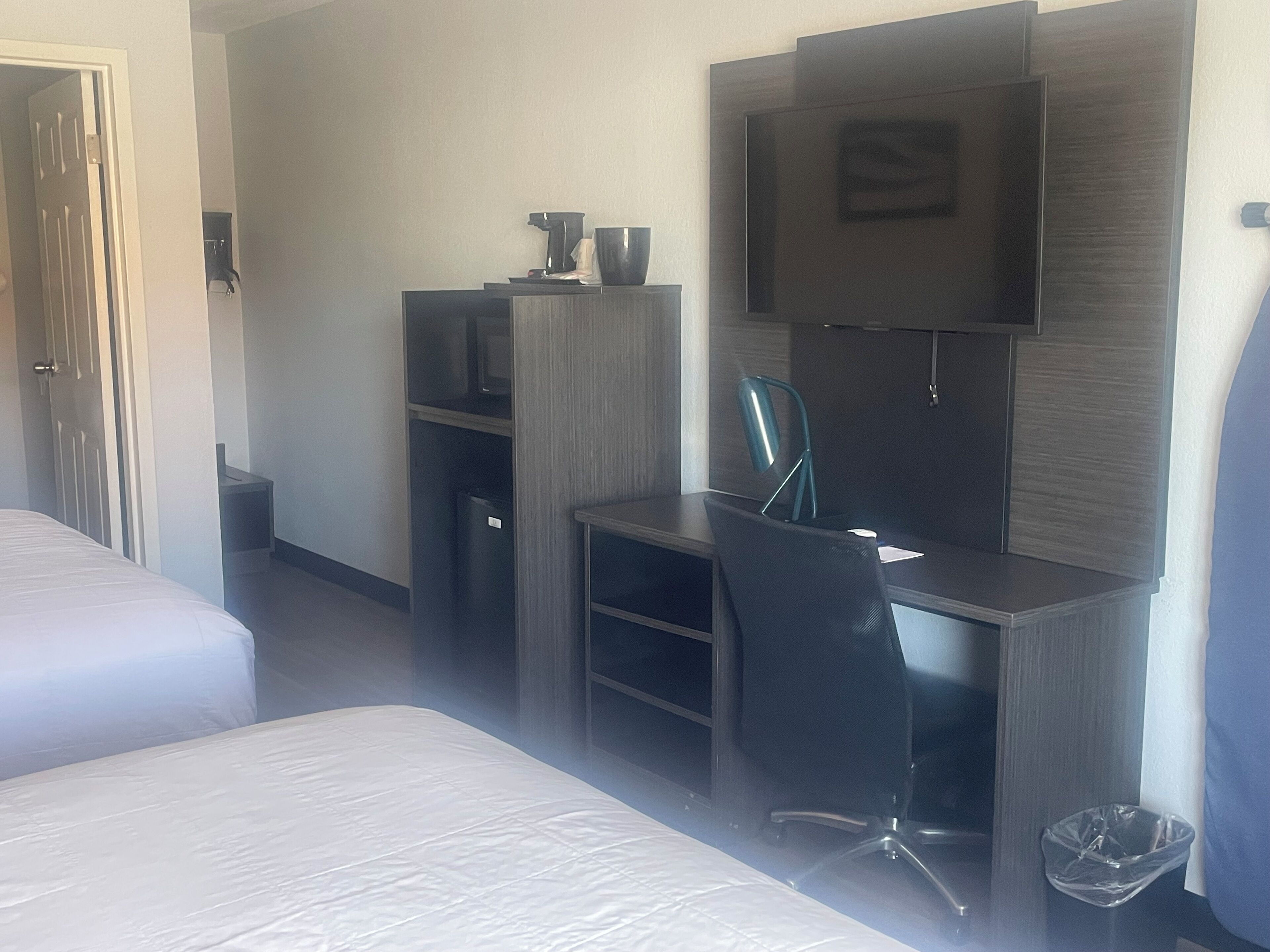 A hotel room with a bed, a desk with a chair, a television, and a trash bin.