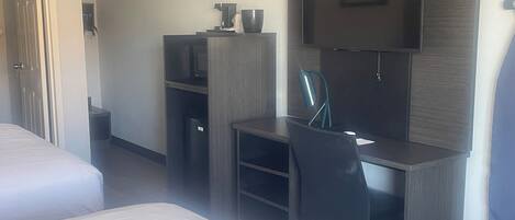 A hotel room with a bed, a desk with a chair, a television, and a trash bin.