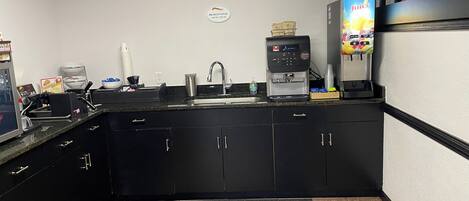 A small kitchen with a coffee machine, a juice dispenser, and a microwave.