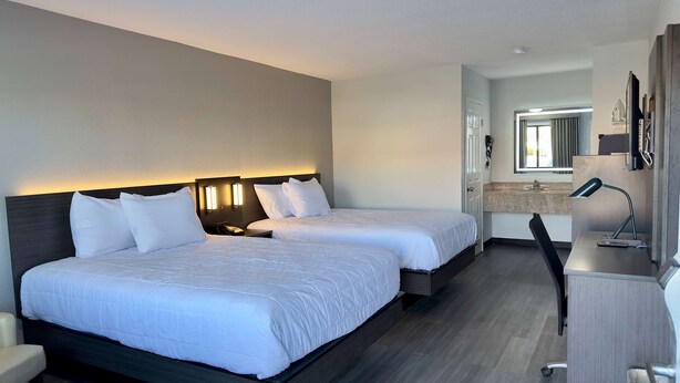 A hotel room with two beds, a desk, and a bathroom visible through an open door.