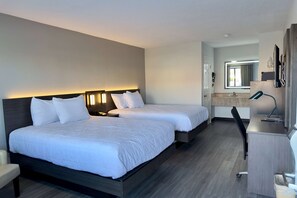 Quarto de hotel com duas camas, uma escrivaninha e um banheiro visível através de uma porta aberta.