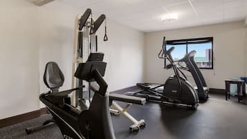 Uma academia com equipamentos de exercícios, uma janela e uma pequena mesa.
