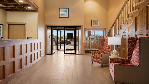 A hotel lobby with a reception desk, a patterned armchair, a staircase, and framed artwork on the walls. - Best Western Kendallville Inn (Kendallville)