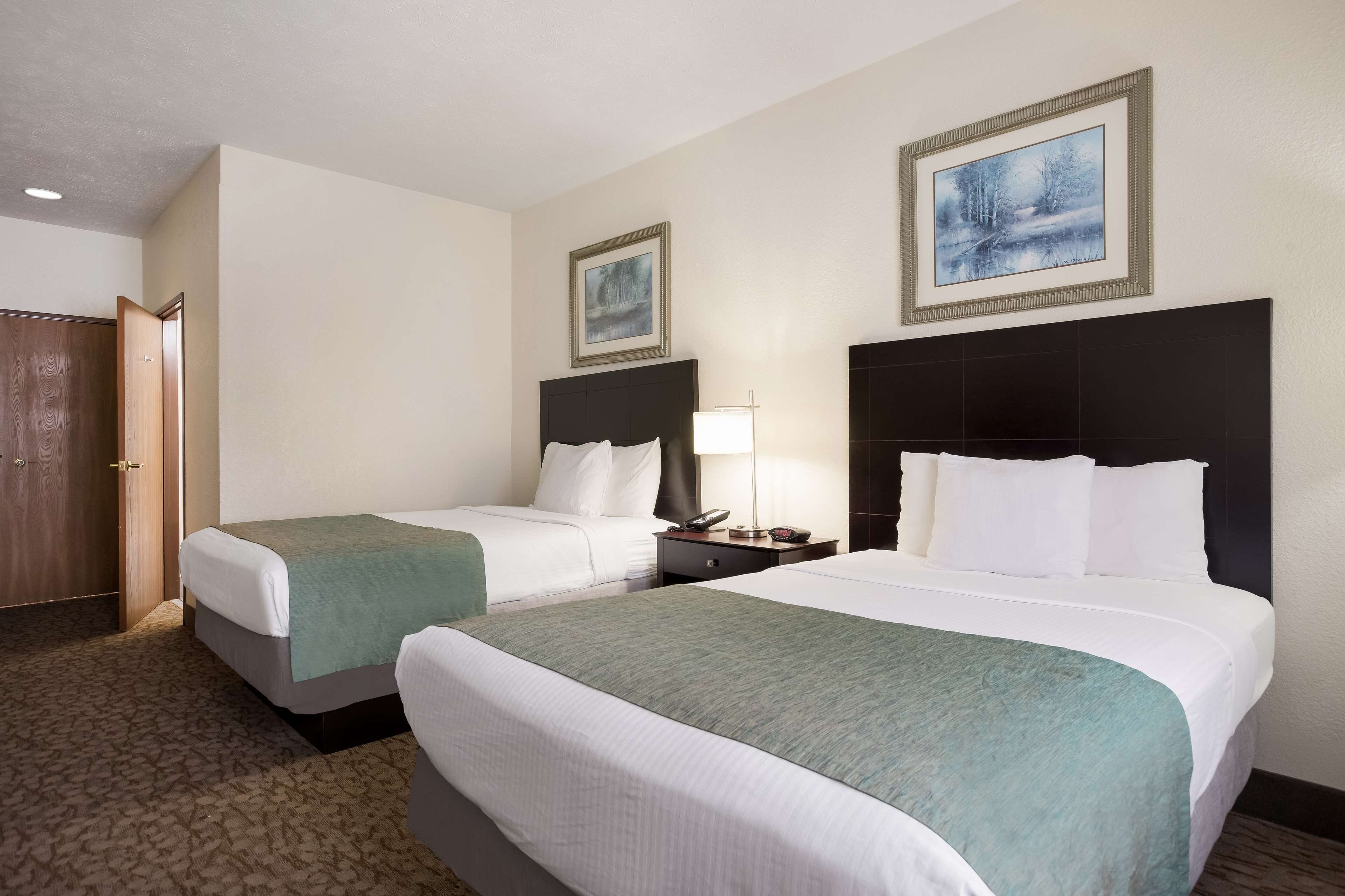 Quarto de hotel com duas camas, uma mesa de cabeceira, um abajur e uma porta.