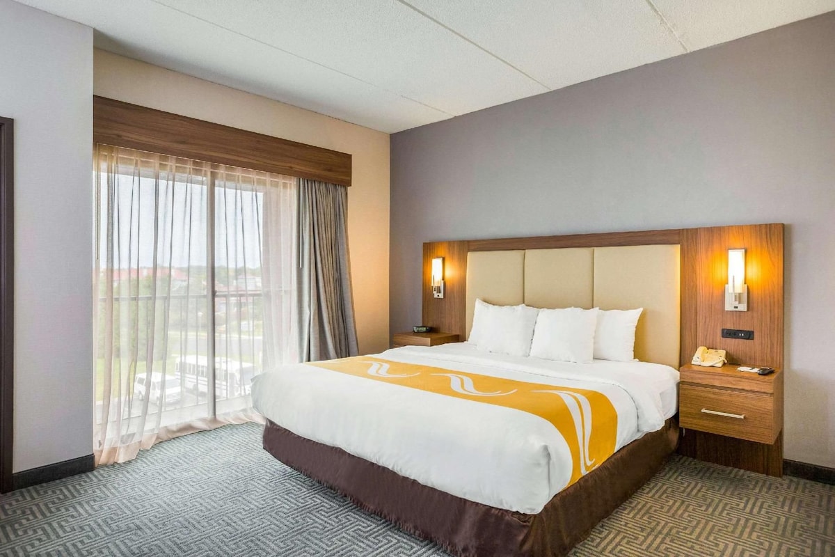 Quarto de hotel com uma cama grande, duas mesas de cabeceira com luminárias, uma janela com cortinas e vista para o exterior.