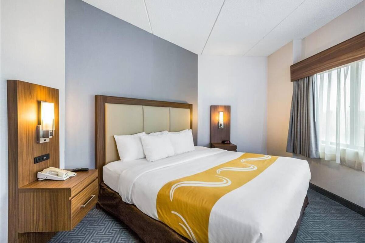 A hotel room with a large bed, a wooden nightstand, a telephone, and a wall-mounted light fixture.