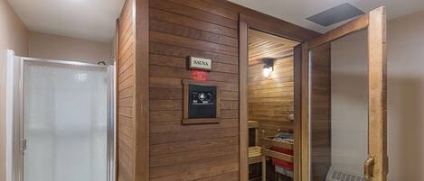 A sauna room with wooden paneling, a control panel, and a glass door.
