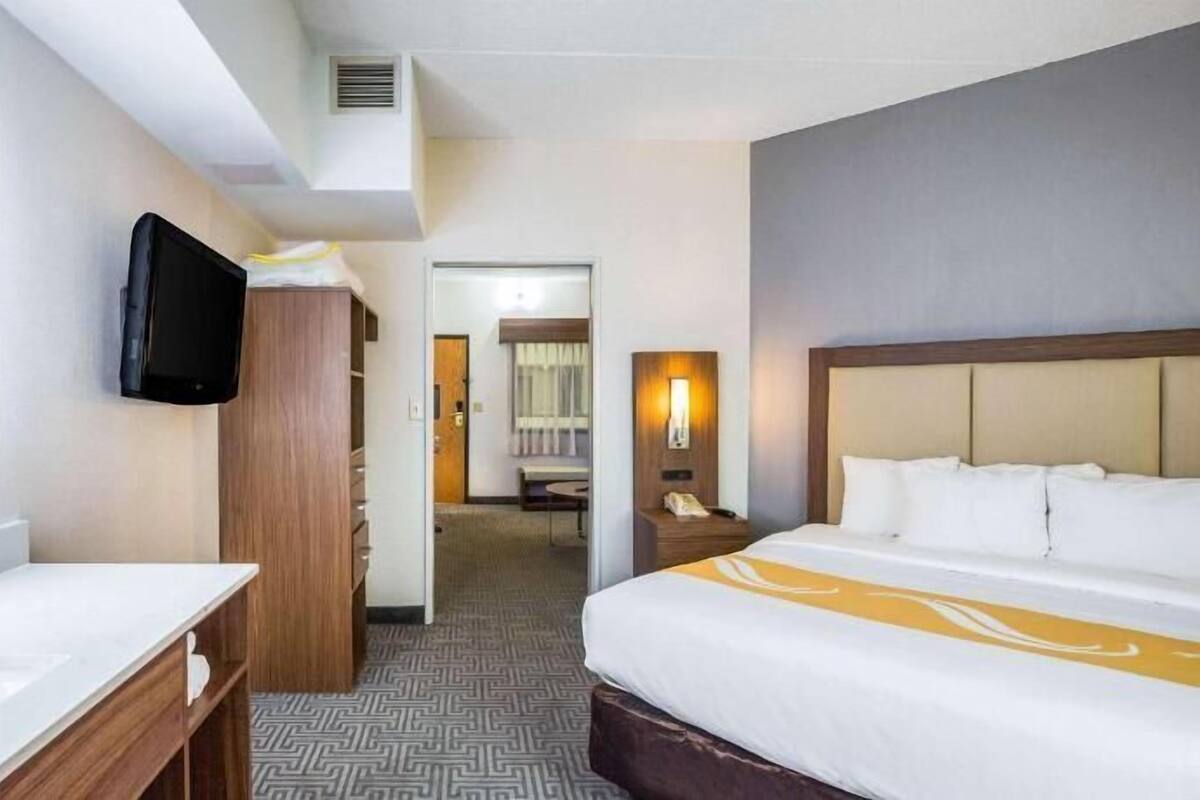 A hotel room with a bed, a TV mounted on the wall, a desk, and a mirror.