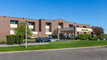 A multi-story hotel with a brick facade, a covered entrance, and a parking lot with several cars.