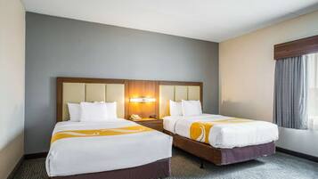 A hotel room with two beds, a large headboard, a nightstand, and a window with curtains.