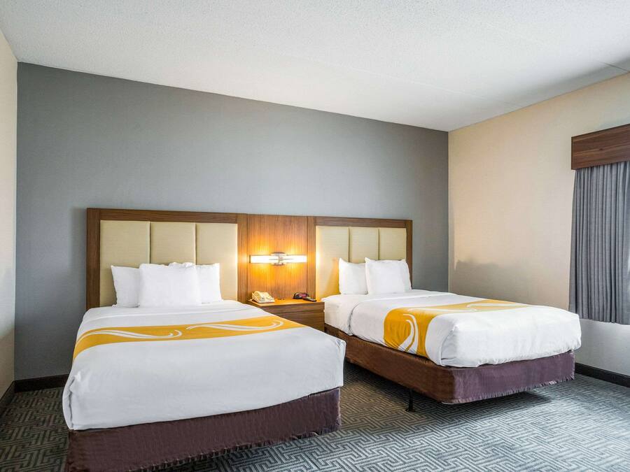 Una habitación de hotel con dos camas, un cabecero grande, una mesita de noche y una ventana con cortinas.
