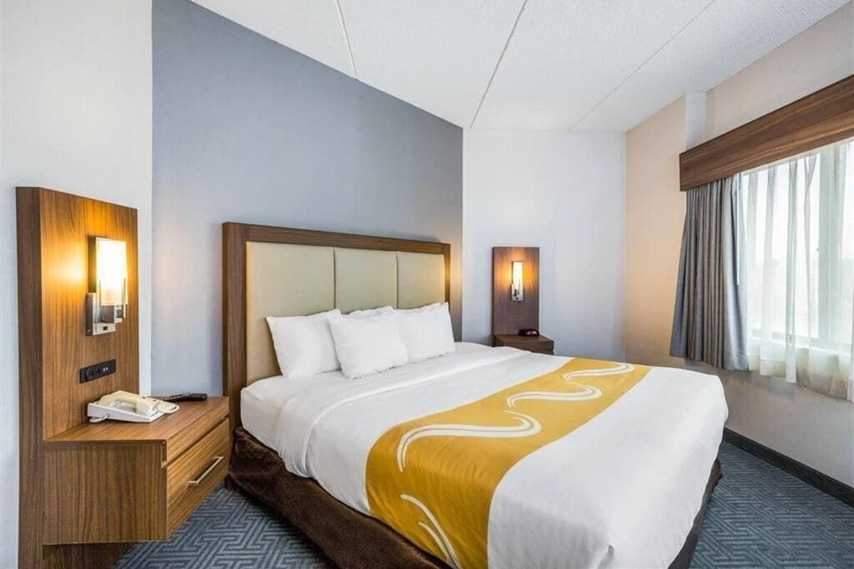 A hotel room with a large bed, bedside tables, a nightstand, a lamp, and a window with curtains.