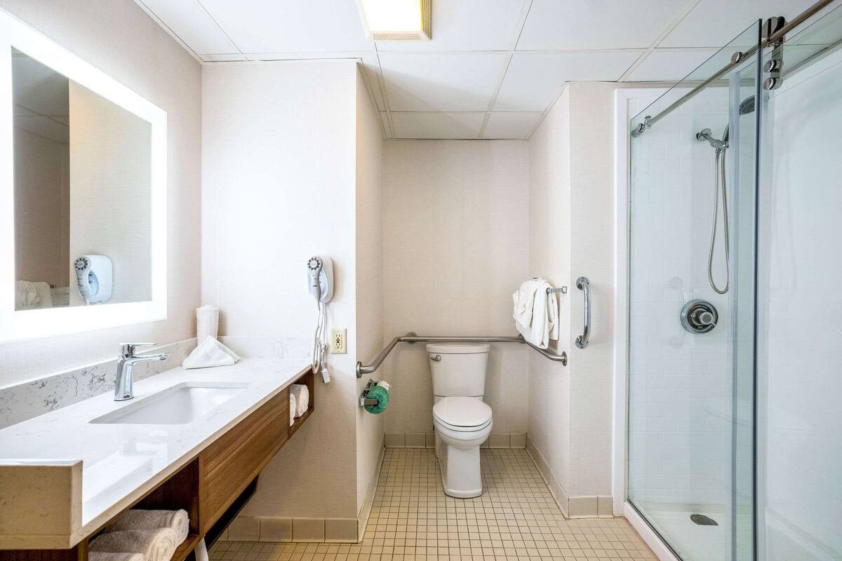 A modern bathroom with a large mirror, a sink, a toilet, and a glass-enclosed shower.