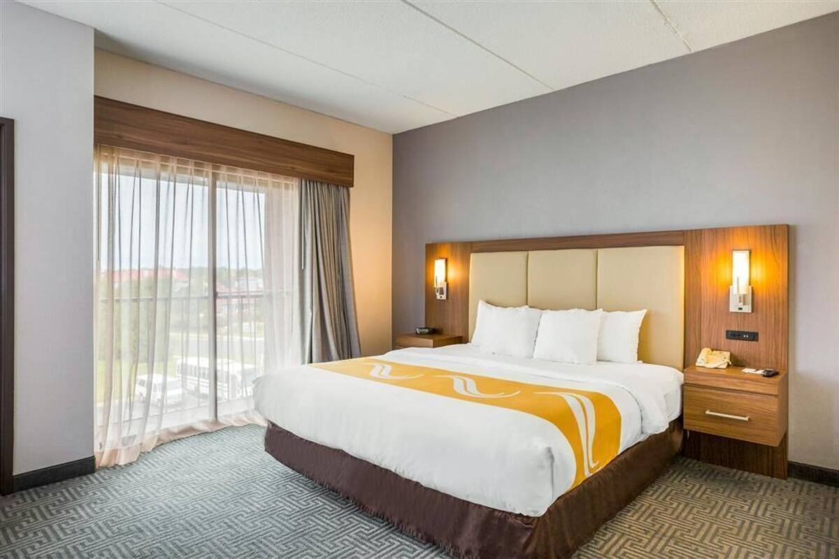 Une chambre d’hôtel avec un grand lit, deux tables de chevet, une commode, une fenêtre avec des rideaux légers et une vue sur l’extérieur.