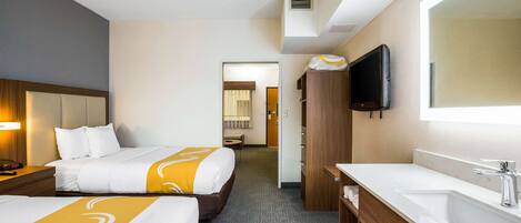 A hotel room with two beds, a bathroom with a sink and mirror, and a TV mounted on the wall.
