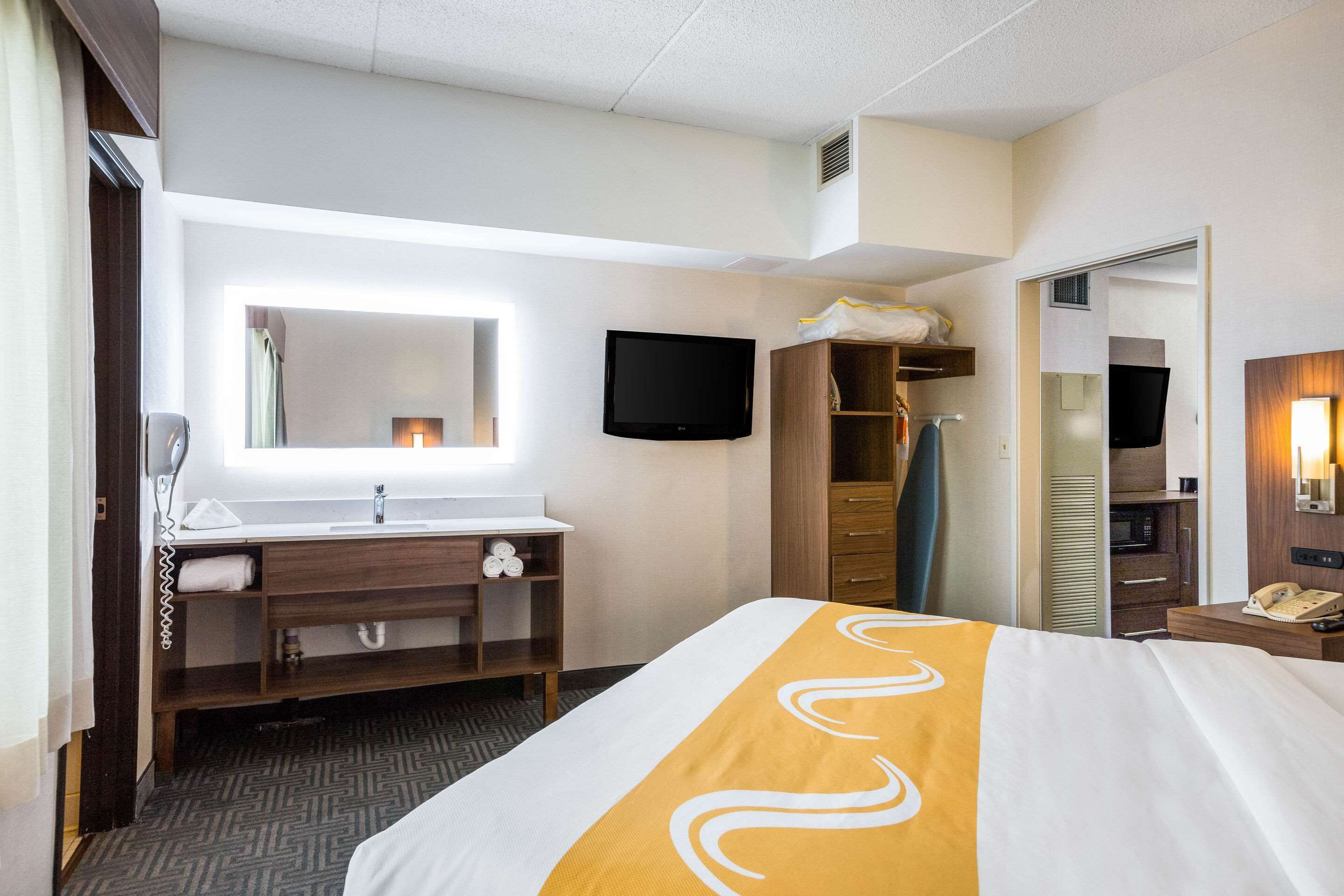 A hotel room with a bed, a desk with a telephone, a mirror, a television, and a wardrobe.