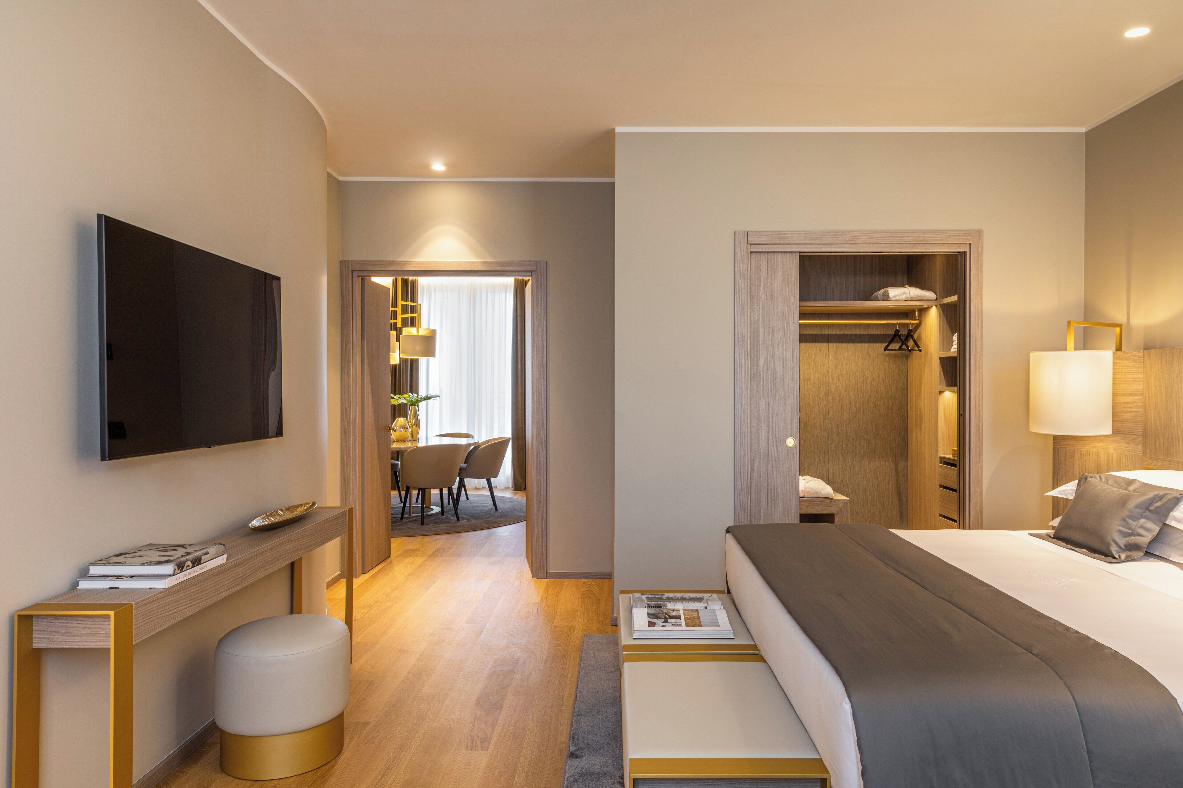 A modern hotel room with a large bed, a TV mounted on the wall, a bedside table, and a walk-in closet.