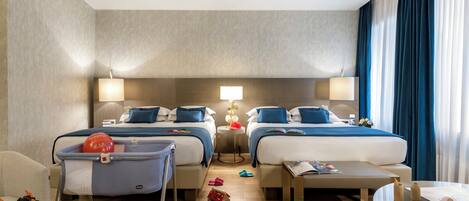 A hotel room with two beds, a small table, a chair, and toys scattered on the floor.