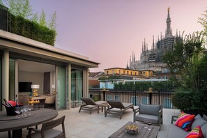 Terraço no telhado com área de refeições, cadeiras de descanso e vista para um edifício histórico.