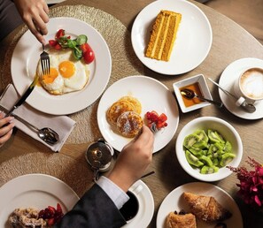 Une table mise pour le petit-déjeuner, avec des assiettes remplies de nourriture, une tasse de café et une théière.