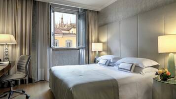 Una camera d'albergo con un letto grande, due lampade sui comodini, una scrivania con una sedia e una finestra che si affaccia su un edificio.