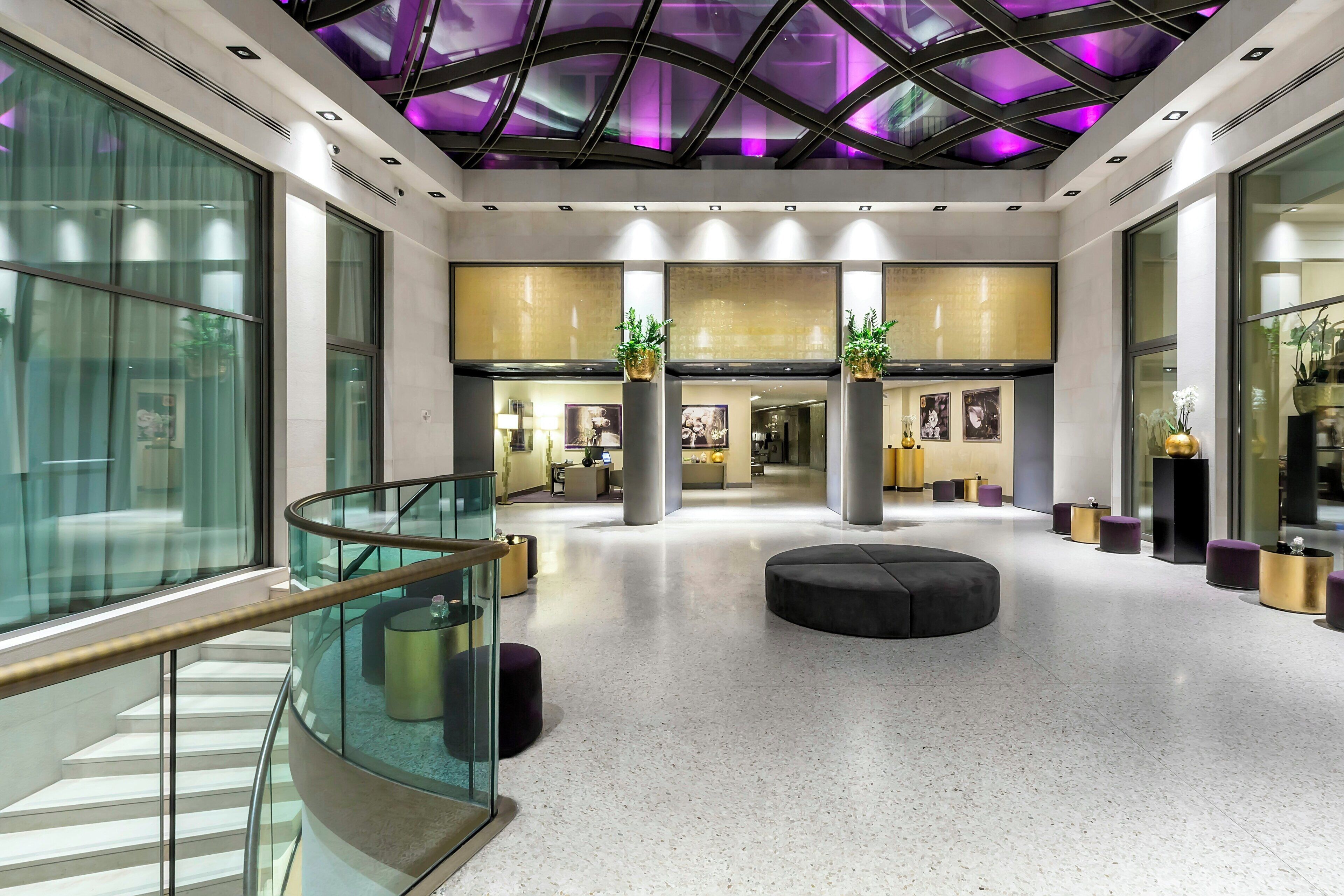 Un hall d’entrée spacieux doté d’un escalier en verre, d’un espace salon central et d’un plafond orné d’un motif géométrique.