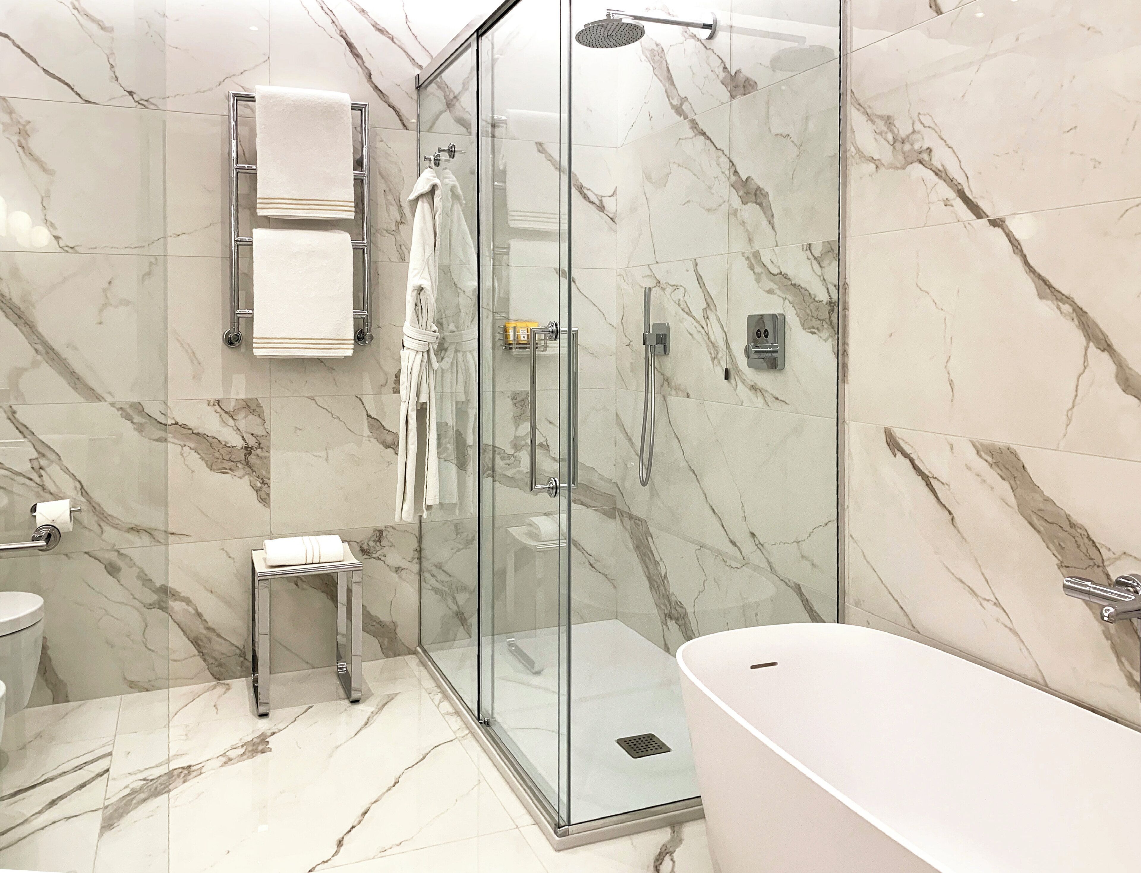 Un bagno moderno con doccia vetrata, vasca da bagno bianca e pavimento in marmo.