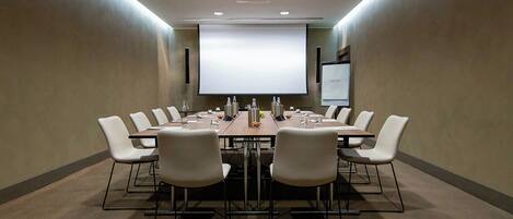 A conference room with a long table, white chairs, a projector screen, and a whiteboard.
