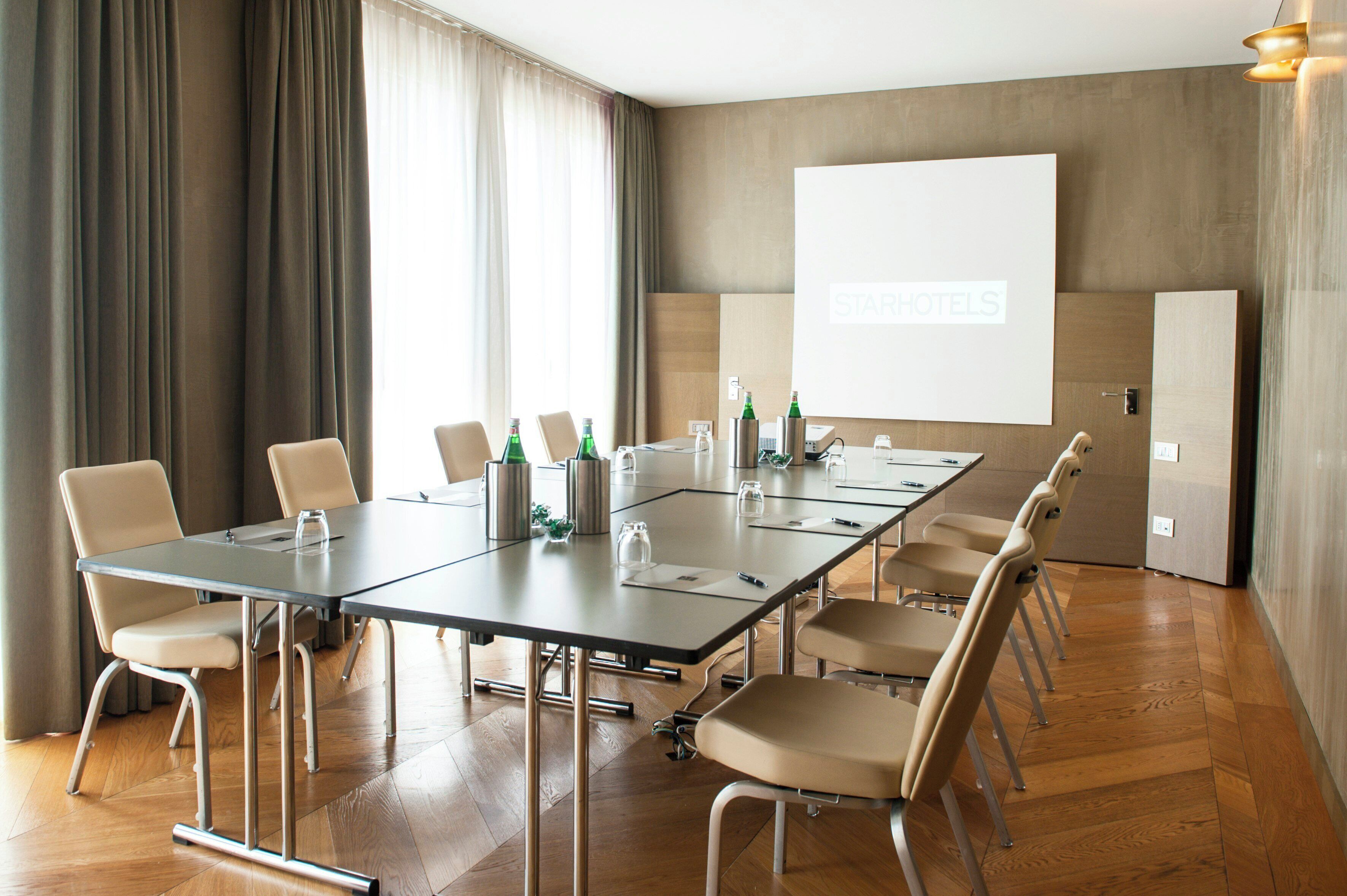 Uma sala de conferências com uma mesa comprida, cadeiras, uma tela de projetor e piso de madeira.