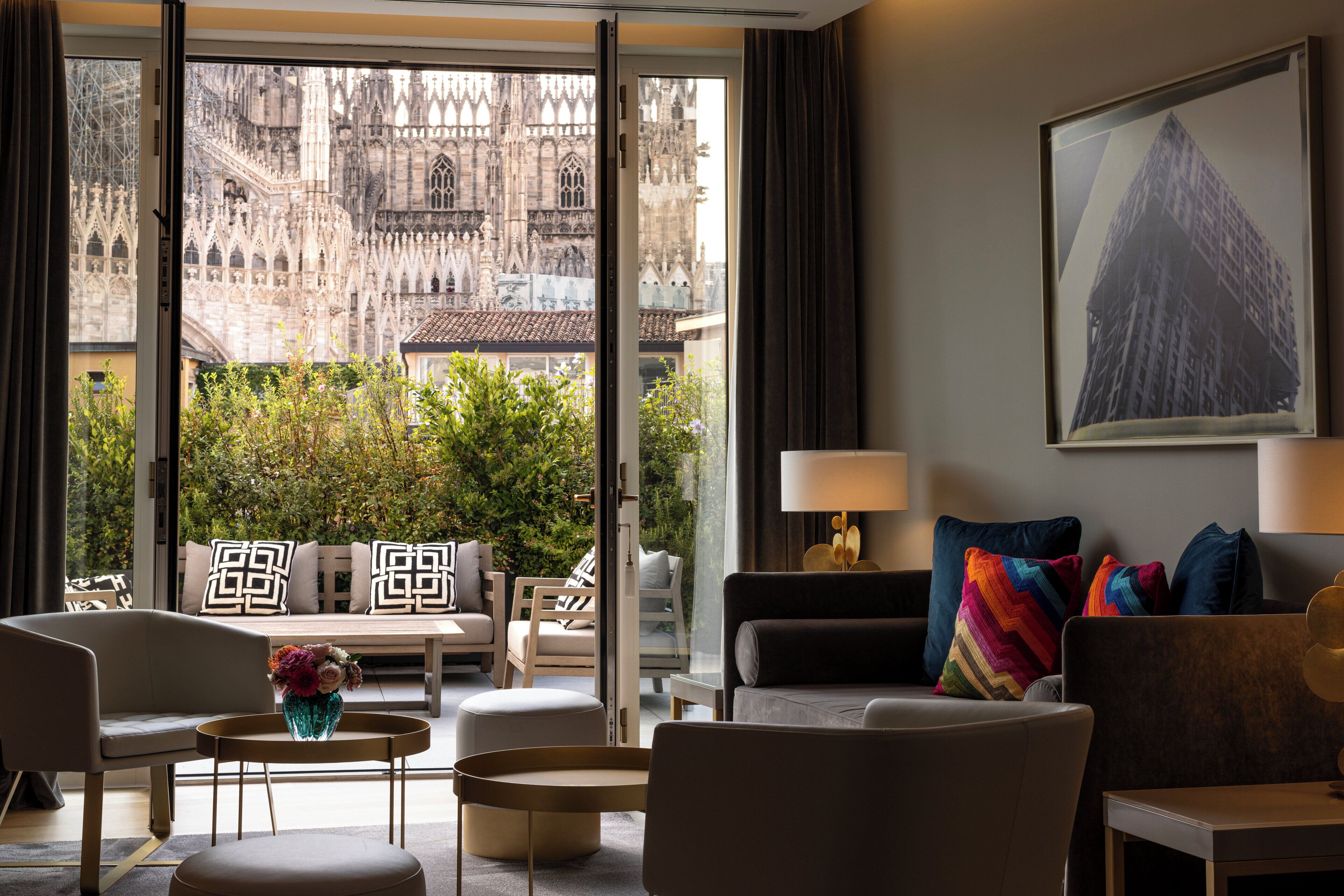 A modern hotel room with a view of a historic cathedral, a comfortable seating area, and a contemporary art piece.