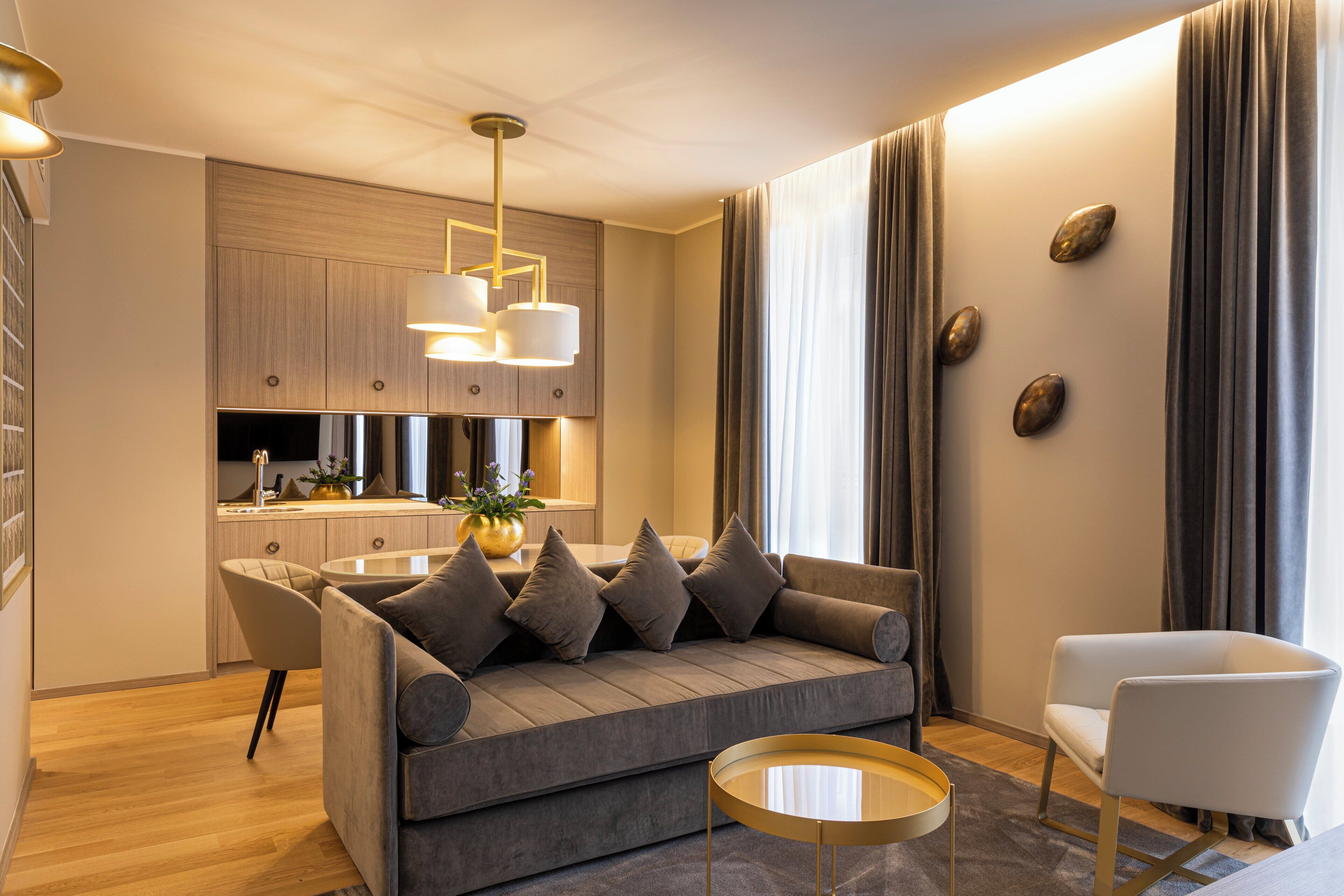 Een moderne woonkamer met een grijze bank, een witte fauteuil, een ronde salontafel, en een keuken in de achtergrond.