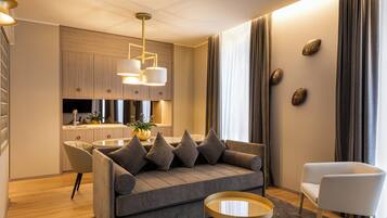 Een moderne woonkamer met een grijze bank, een witte fauteuil, een ronde salontafel, en een keuken in de achtergrond.