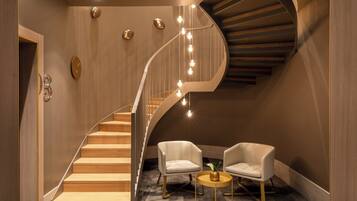 Un intérieur moderne avec un escalier en bois, deux fauteuils blancs, une petite table ronde et une horloge murale.