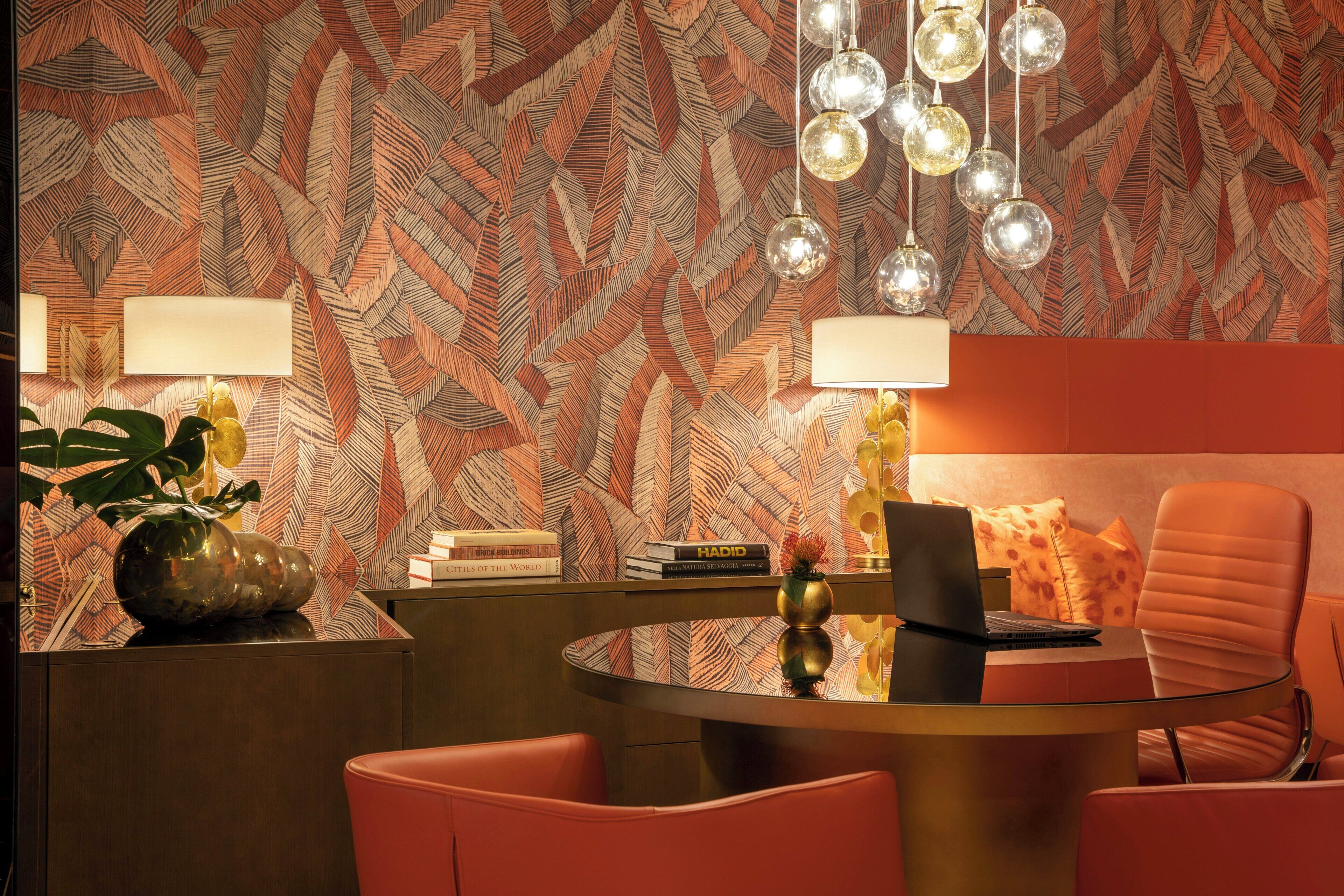 A modern room with a patterned wallpaper, a round glass table, a laptop, a chair, and a lamp.