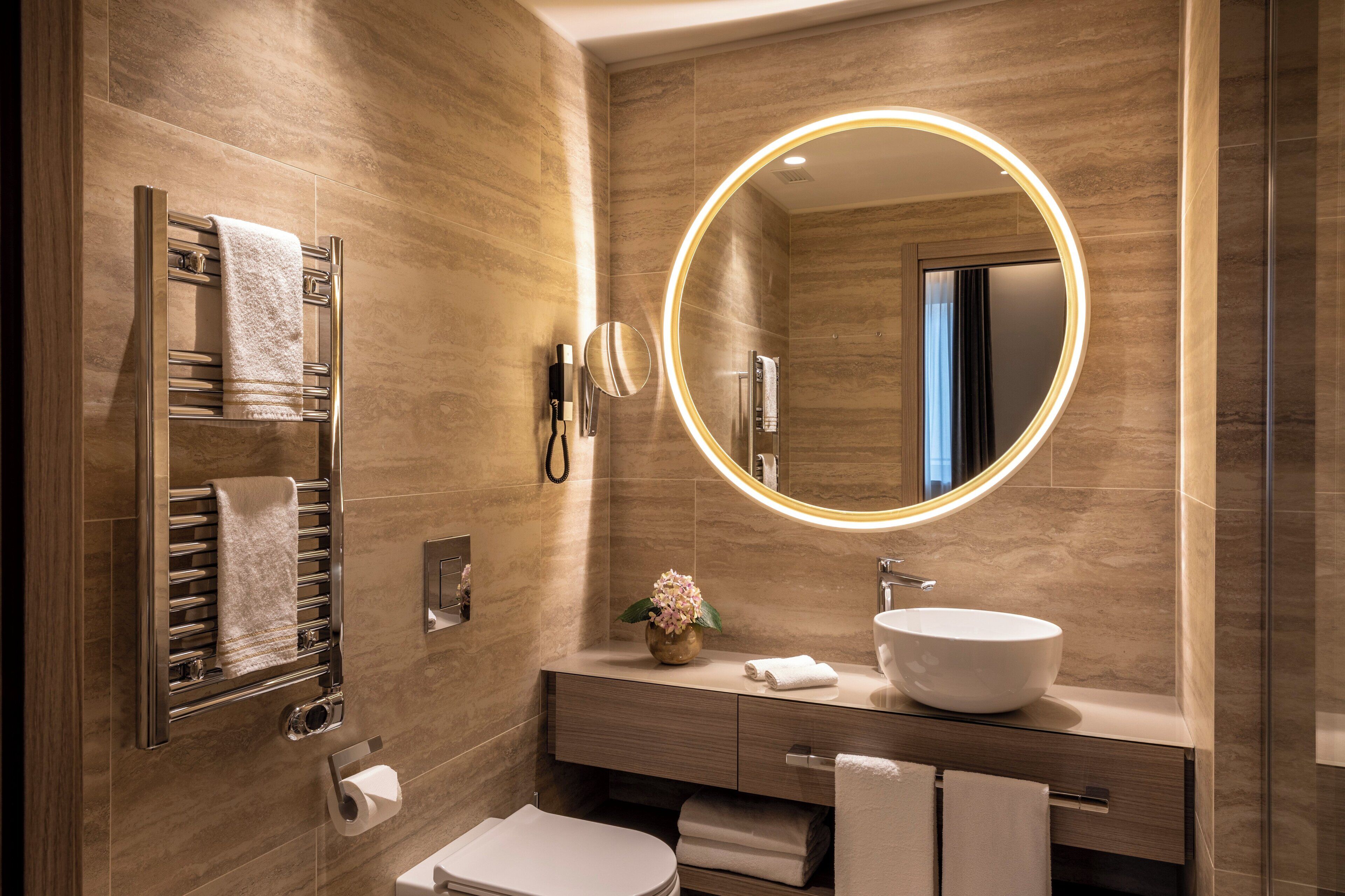 A modern bathroom with a large mirror, a towel rack, a sink, and a toilet.