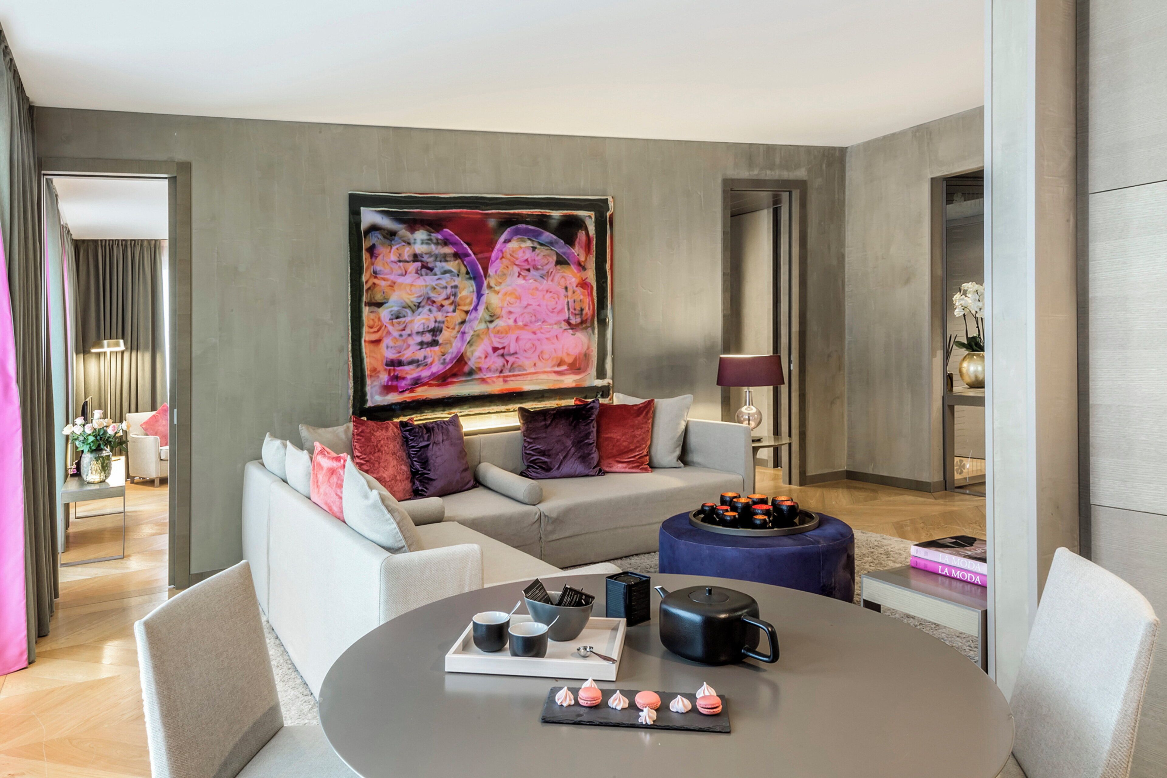 Uma sala de estar moderna com um sofá cinzento, uma mesa de centro com uma bandeja de petiscos e um grande quadro abstrato na parede.