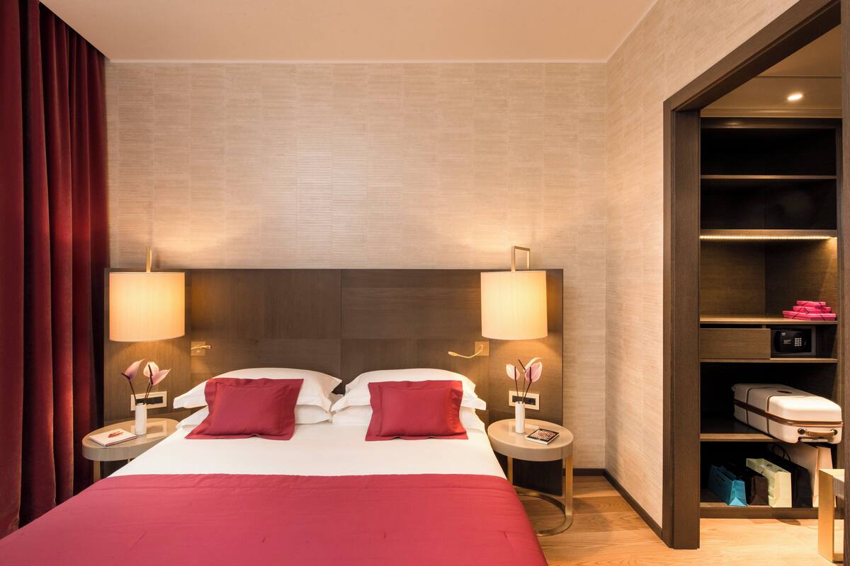 Une chambre d’hôtel avec un grand lit, deux tables de chevet avec des lampes, une armoire intégrée et un rideau rouge.