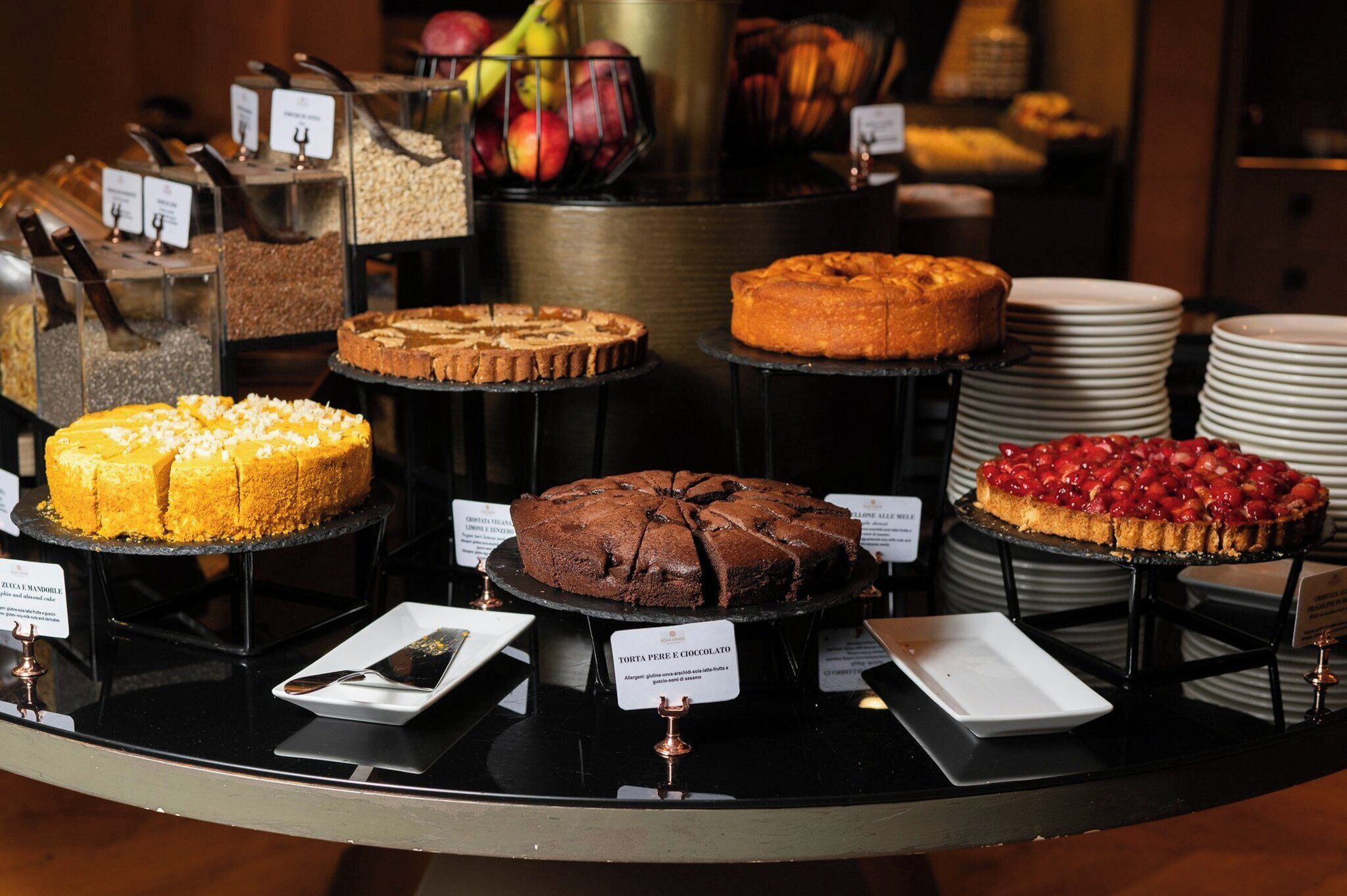 A display of various cakes and pastries on a counter with labels.