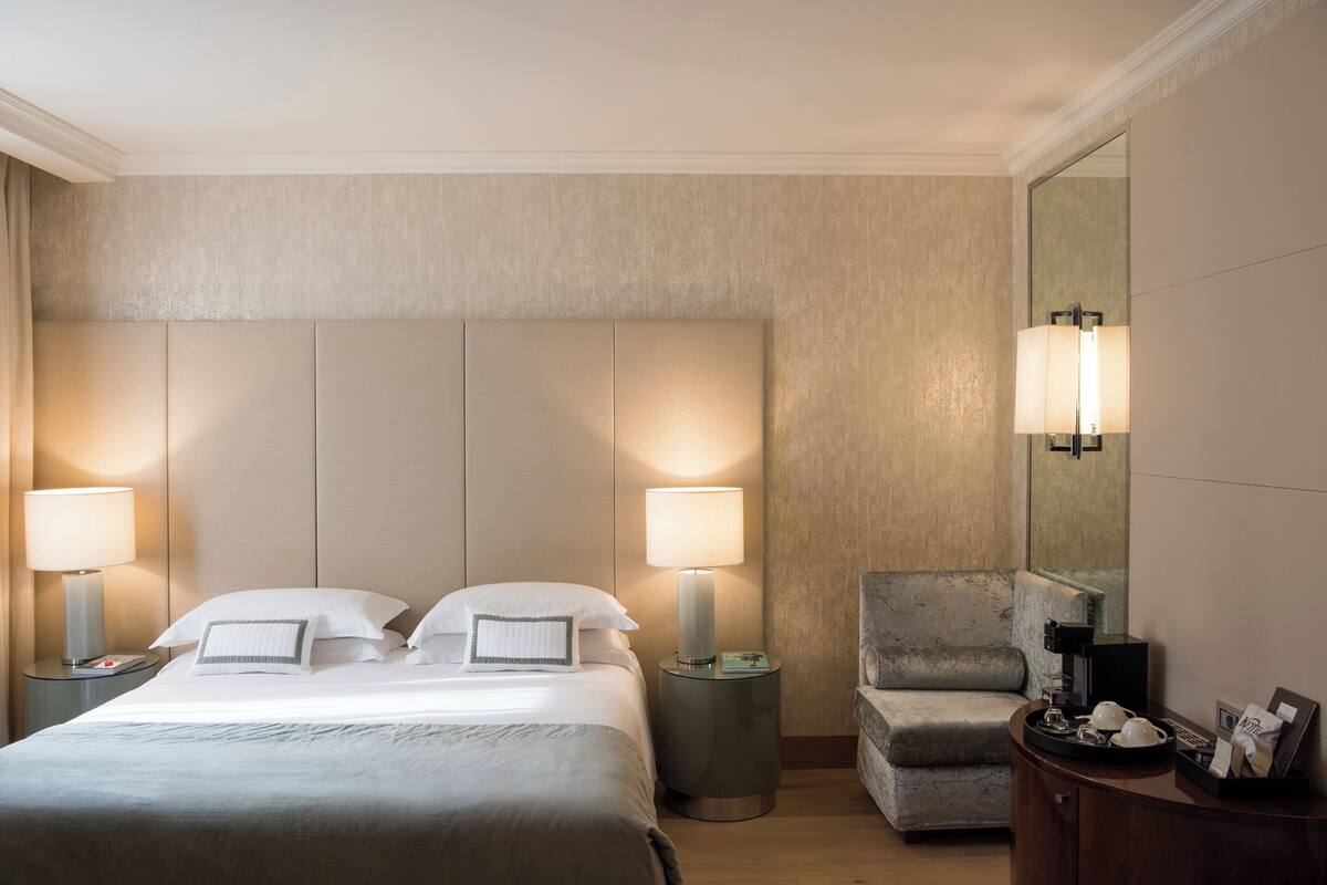 Une chambre d’hôtel avec un grand lit, deux lampes de chevet, une chaise, une petite table et un miroir.