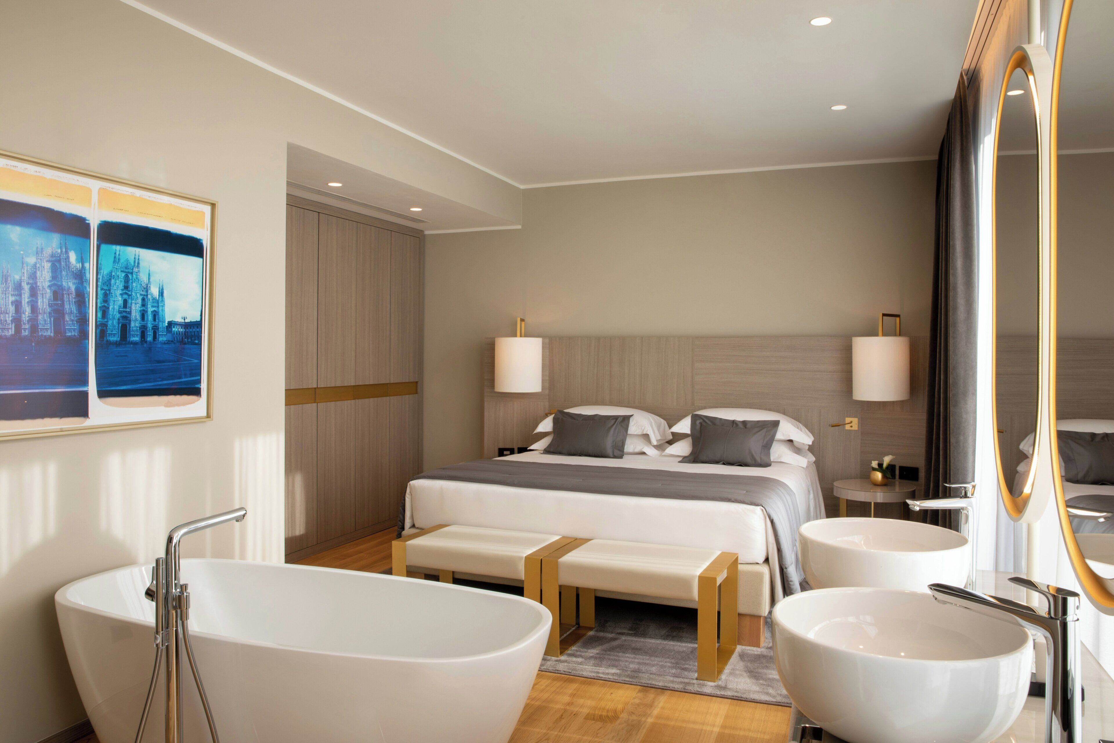 Une chambre d’hôtel moderne dotée d’un grand lit, de deux tables de chevet, d’un coin salon, d’une baignoire et d’un grand miroir.