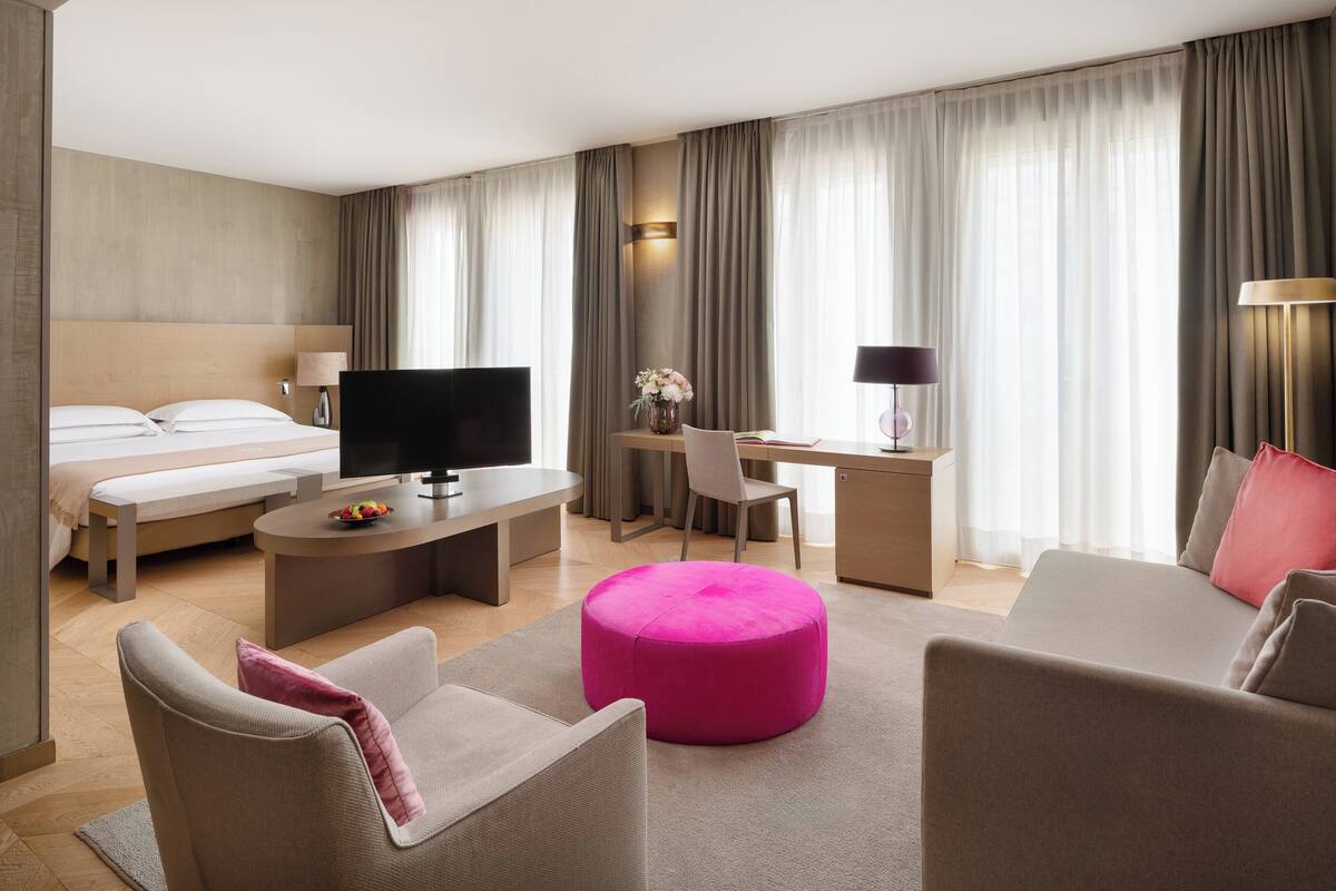 Une chambre d’hôtel avec un lit, une télévision, un bureau, une chaise et un pouf rose.
