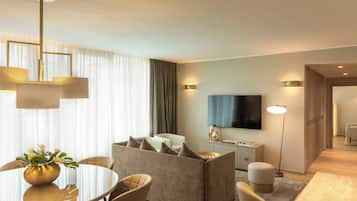 A modern hotel room with a sofa, dining table, and a flat-screen TV.