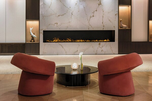 Un hall d’entrée moderne avec une cheminée, deux fauteuils rouges et une table basse en verre.