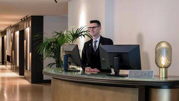 A reception desk with a 'CONCIERGE' sign, a computer monitor, a plant, and a decorative lamp.