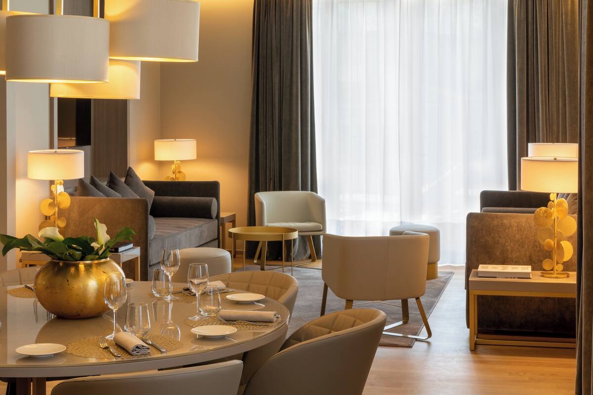 Une chambre d’hôtel avec une table à manger ronde, dressée pour quatre personnes, un canapé, un fauteuil et une petite table d’appoint avec une lampe.