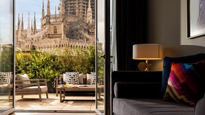 A hotel room with a large window offering a view of a historic cathedral under construction. Inside, there is a sofa, a small table, and a lamp. - Rosa Grand Milano - Starhotels Collezione (Milan)