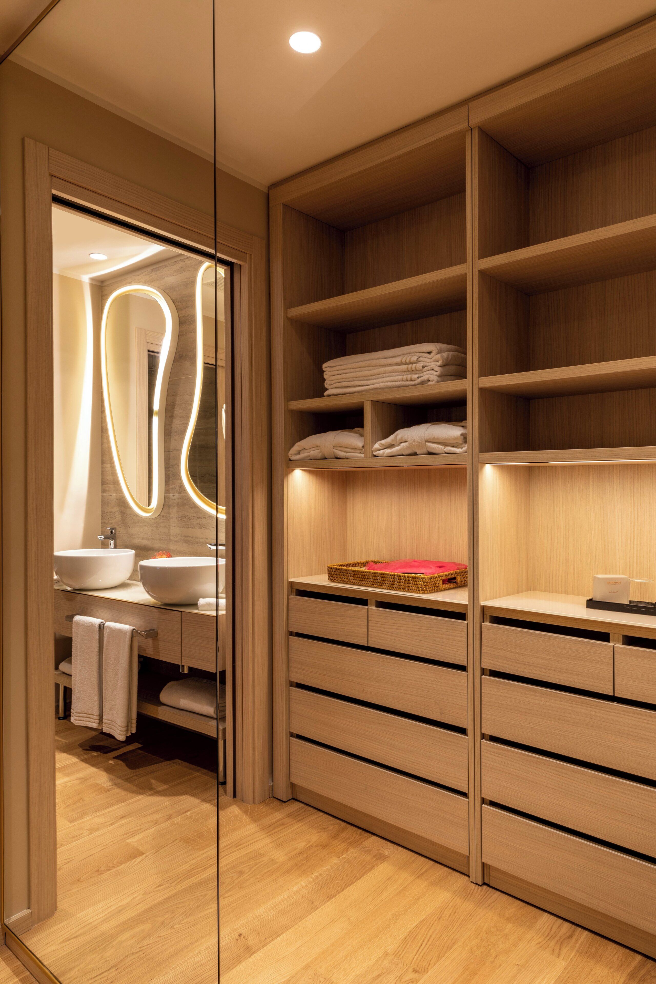 Een moderne badkamer met een houten wastafelmeubel, een grote spiegel en inbouwplanken.