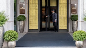 The entrance to Rosa Grand hotel with a man in uniform at the door, potted plants, and a sign above the entrance. - Rosa Grand Milano - Starhotels Collezione (Milan)