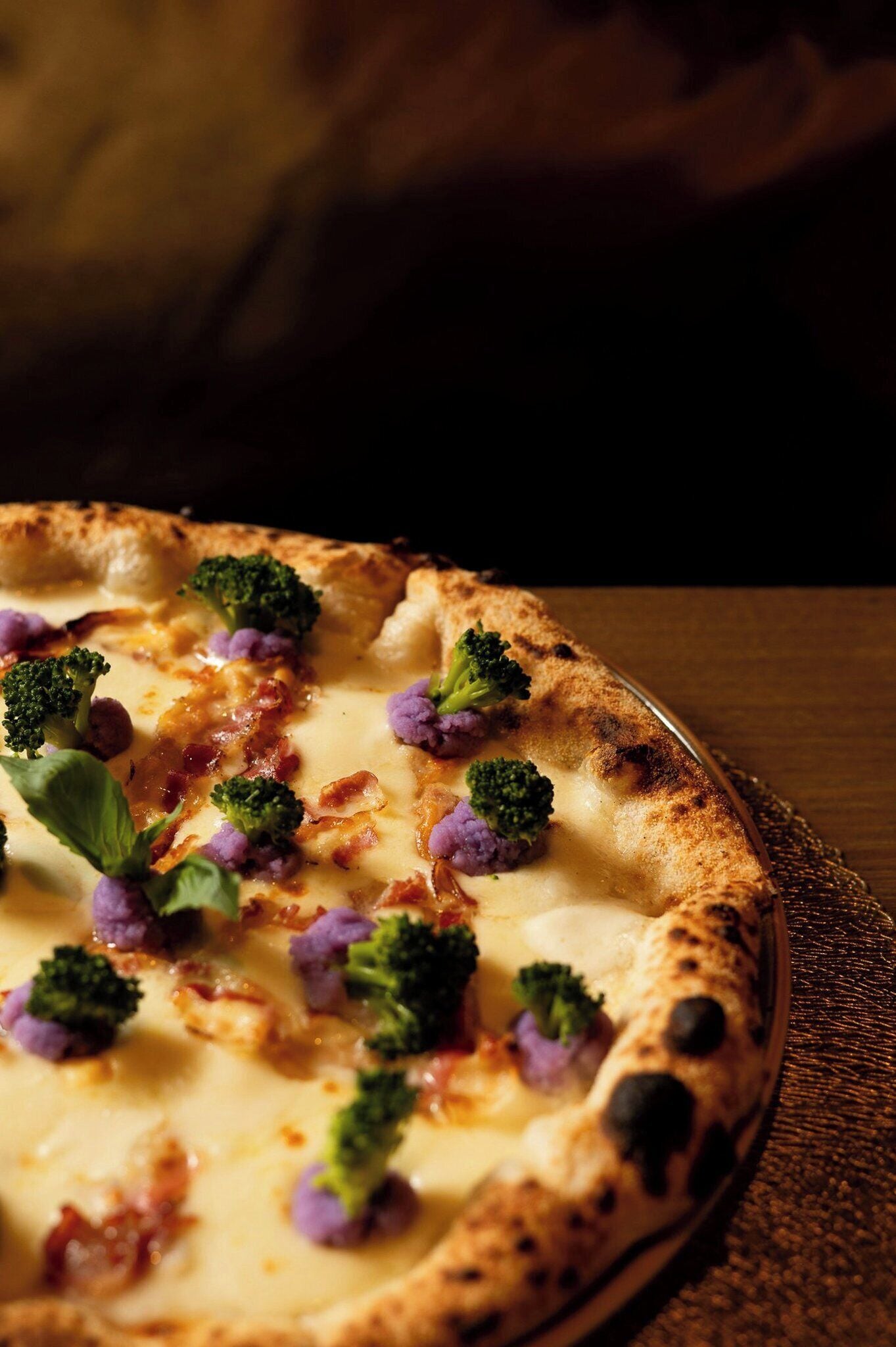 A pizza with broccoli and cheese on a wooden table.