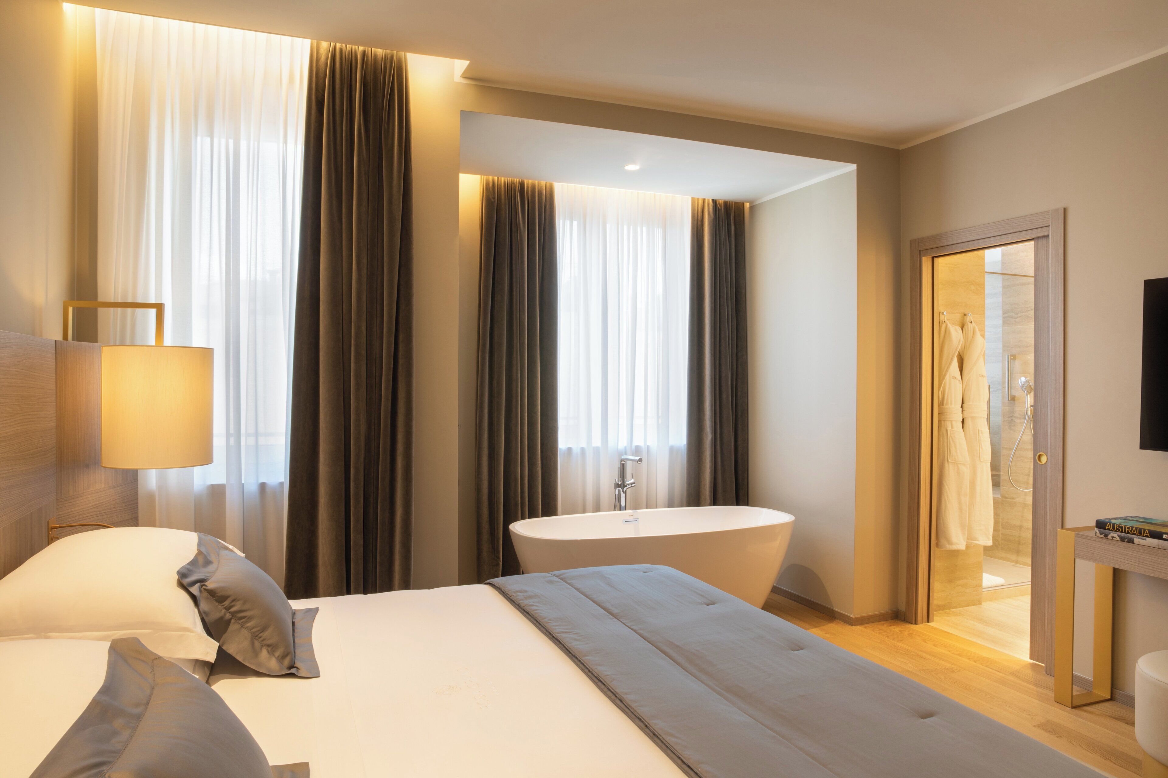 A modern hotel room with a large bed, a bathtub, and a separate shower area.